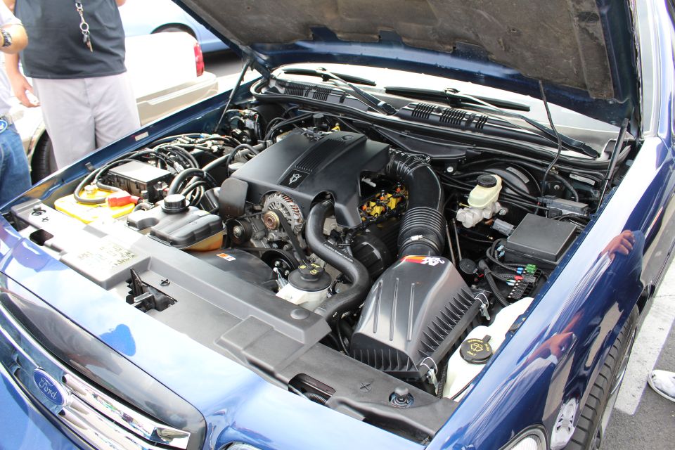 Engine bay of a blue Ford sedan with K&N intake at a car show