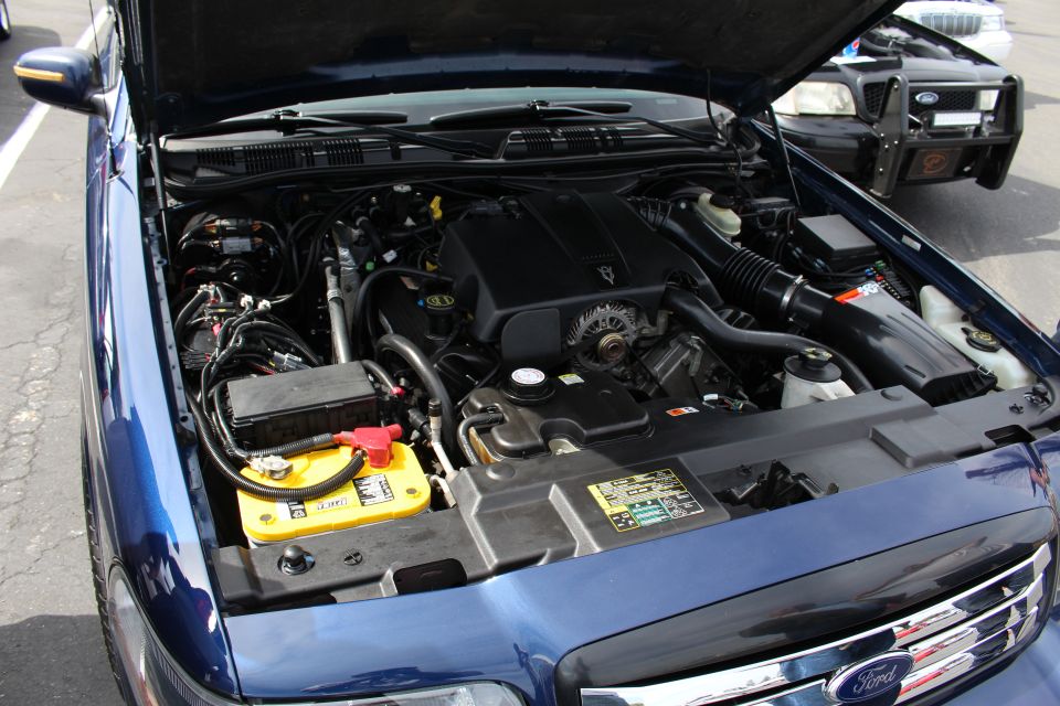Engine bay of a dark blue Ford sedan with yellow battery