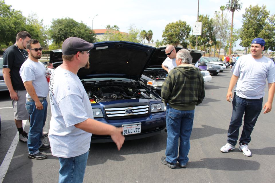 People around a blue Ford sedan with BLUE VIC plate at car show