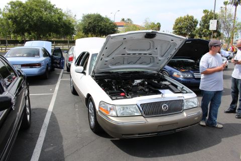 Gold Mercury Grand Marquis sedan, hood open, with onlookers nearby