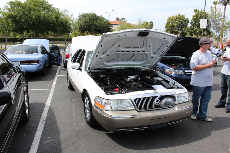Gold Mercury Grand Marquis sedan, hood open, with onlookers nearby