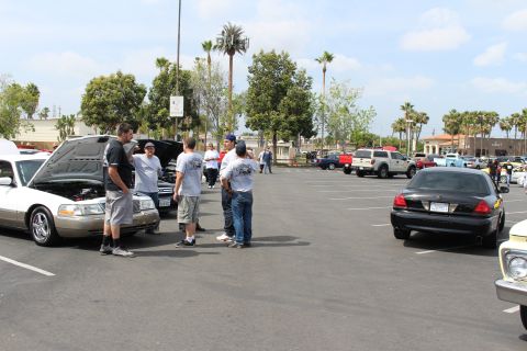 Spectators around a gold Mercury sedan with hood raised in a lot