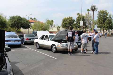 White sedan with open hood surrounded by people at a car meet