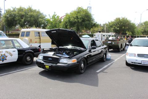 Black Ford Crown Victoria, hood up, beside CHP car and military trailer