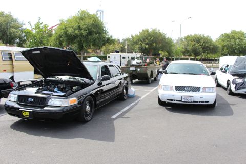 Black Ford Crown Victoria with open hood next to a white Ford sedan