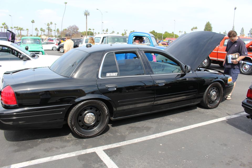 Black Ford Crown Victoria with steel wheels and open hood at a meet