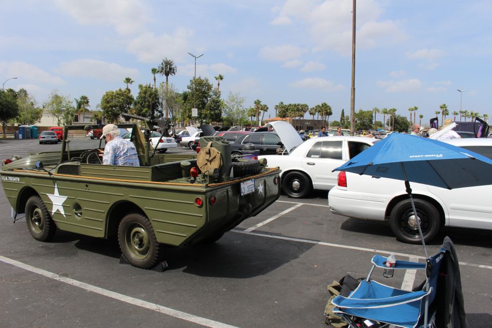 Olive-green military jeep with mounted machine gun beside white sedans in a lot