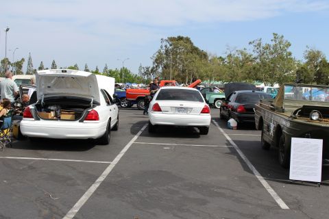 Rear view of two white sedans with open trunks parked in a sunny lot