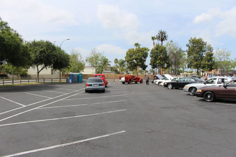 Sparsely parked cars and a red tractor across a large empty asphalt lot