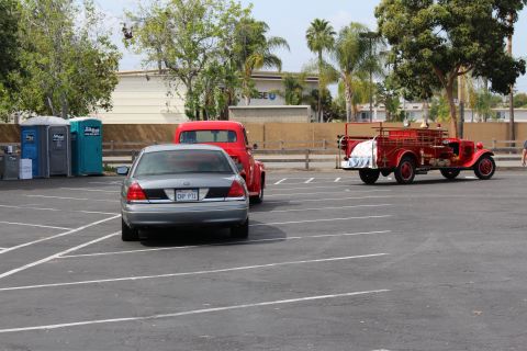 Vintage red fire engine parked near a silver sedan and portable toilets