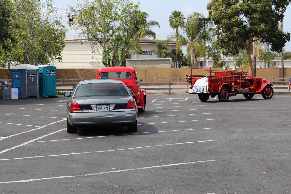 Vintage red fire engine parked near a silver sedan and portable toilets