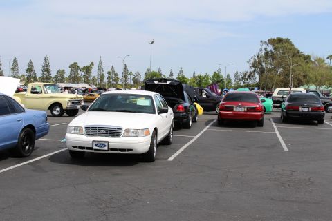 White Ford sedan facing camera among parked cars at a sunny car show
