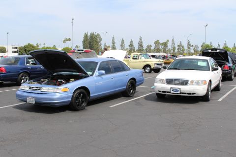 Light-blue Ford sedan with open hood beside a white Ford sedan in a lot