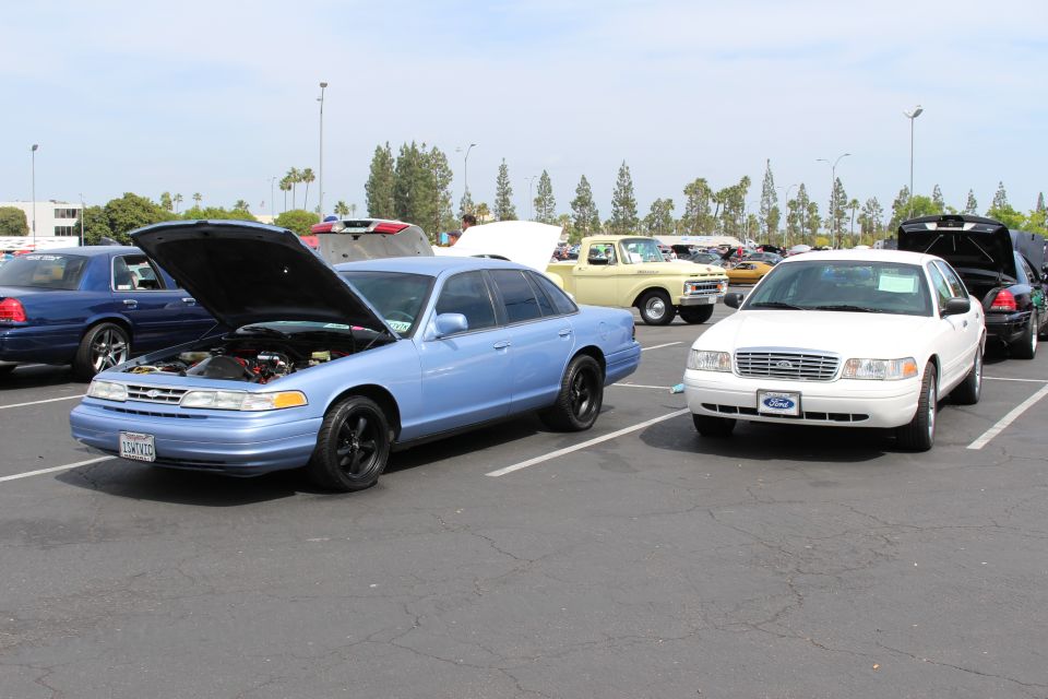 Light-blue Ford sedan with open hood beside a white Ford sedan in a lot
