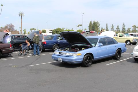 Light-blue sedan with open hood and people standing in a parking lot