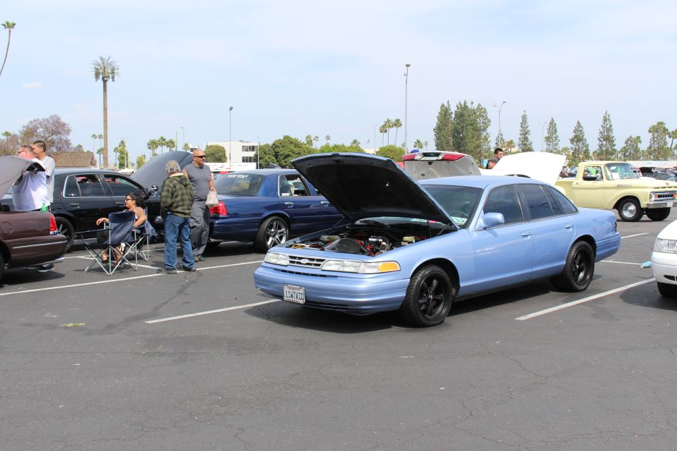 Light-blue sedan with open hood and people standing in a parking lot