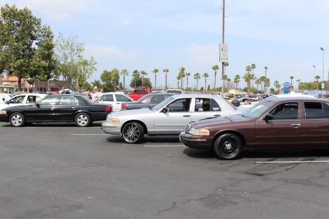 Black, silver and brown sedans parked in a row at a sunny car show