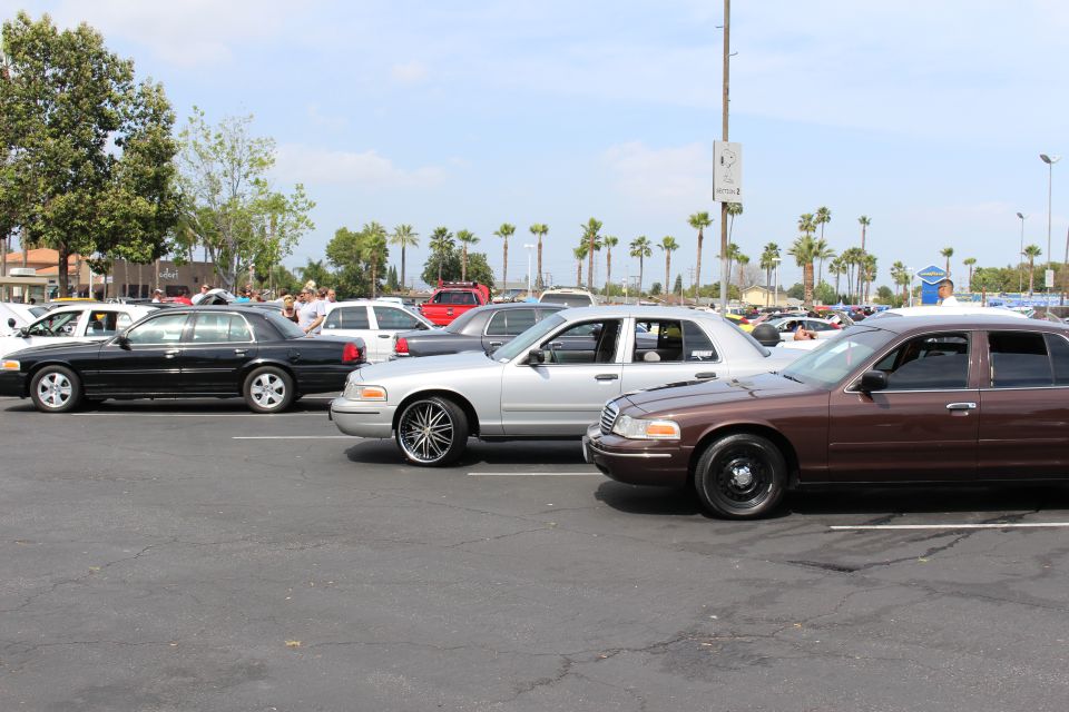 Black, silver and brown sedans parked in a row at a sunny car show