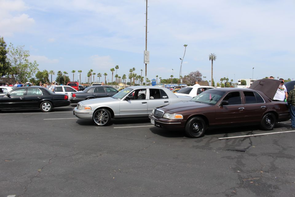 Silver and brown full-size sedans on chrome wheels at an outdoor car meet