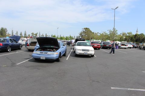Light-blue sedan with open hood beside a white sedan in a sunny lot