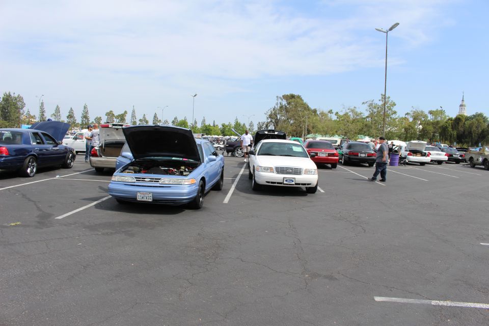 Light-blue sedan with open hood beside a white sedan in a sunny lot