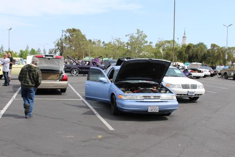 Light-blue Ford sedan with open doors and hood beside a white Ford sedan