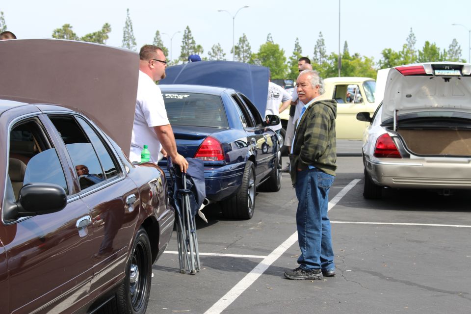 Men talking between a brown sedan and a dark blue sedan in a parking lot