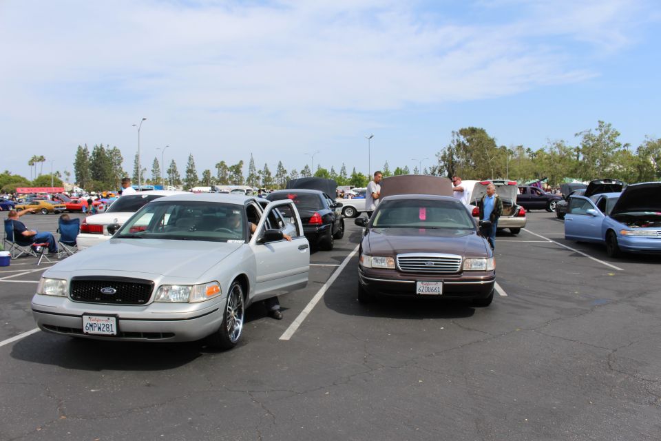 Silver Ford sedan with open door beside a brown sedan at a crowded car show parking lot