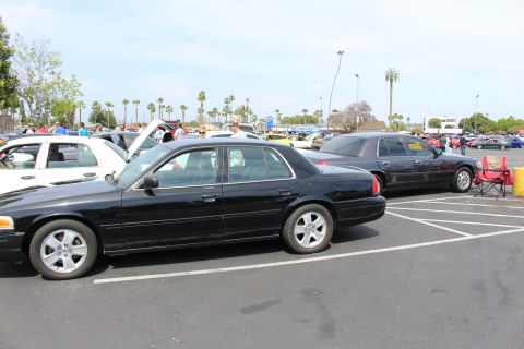 Black sedans parked in marked spaces with a red folding chair and crowd in the background
