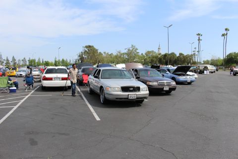 Silver Ford sedan with chrome wheels parked among sedans in a large lot, person standing nearby