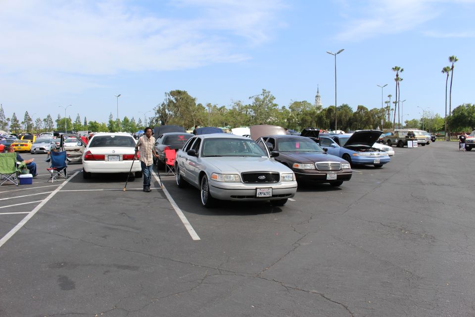 Silver Ford sedan with chrome wheels parked among sedans in a large lot, person standing nearby