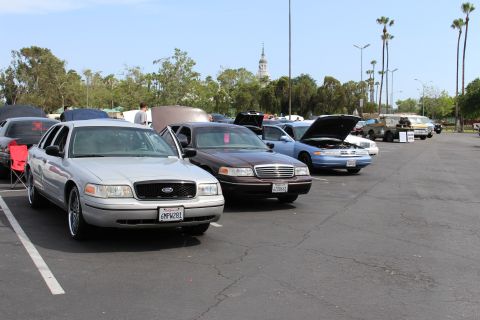 Silver Ford sedan beside a brown sedan and others with raised hoods, tower in the distance