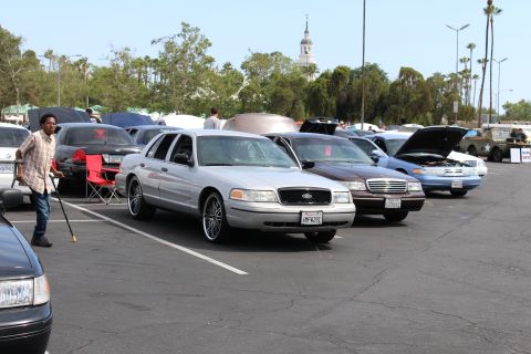 Silver Ford sedan with chrome wheels in a row of cars, man with cane walking nearby