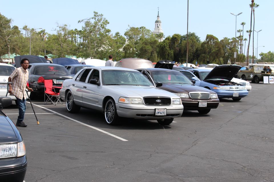 Silver Ford sedan with chrome wheels in a row of cars, man with cane walking nearby