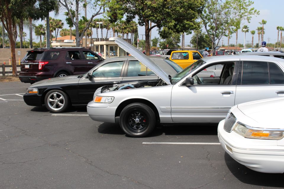 Silver sedan with raised hood and black wheels between a black sedan and a white sedan