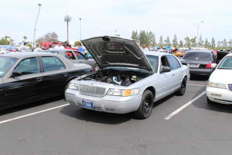 Silver sedan with open hood and a vanity plate reading KAGE, parked among many cars