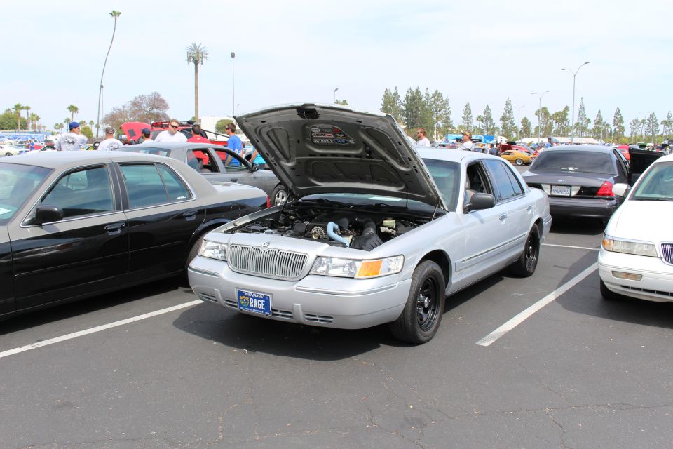 Silver sedan with open hood and a vanity plate reading KAGE, parked among many cars