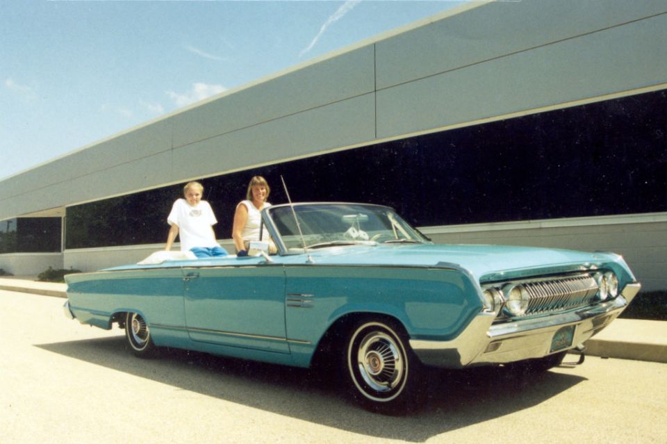 Blue 1964 Mercury Monterey convertible parked outside a modern building