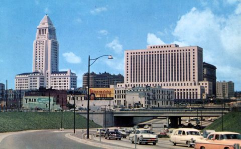 1991 Ford LTD Crown Victoria - View of downtown Los Angeles, including City Hall, with cars driving on a freeway.