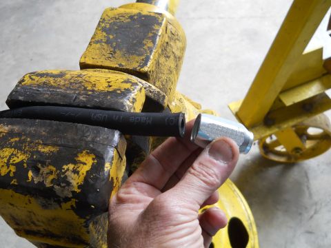 1992 Ford Bronco - A hand holds a metal fitting next to a black hose secured in a yellow vise.
