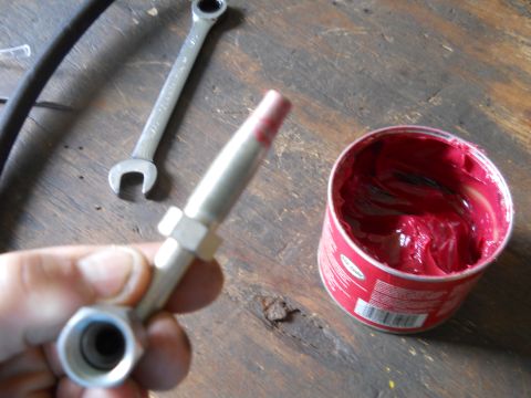 1992 Ford Bronco - A grease gun fitting is held in hand next to a wrench and a can of red grease, suggesting maintenance work.