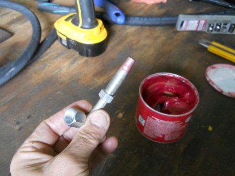 1992 Ford Bronco - A threaded rod is being greased with red lubricant next to its container on a workbench.