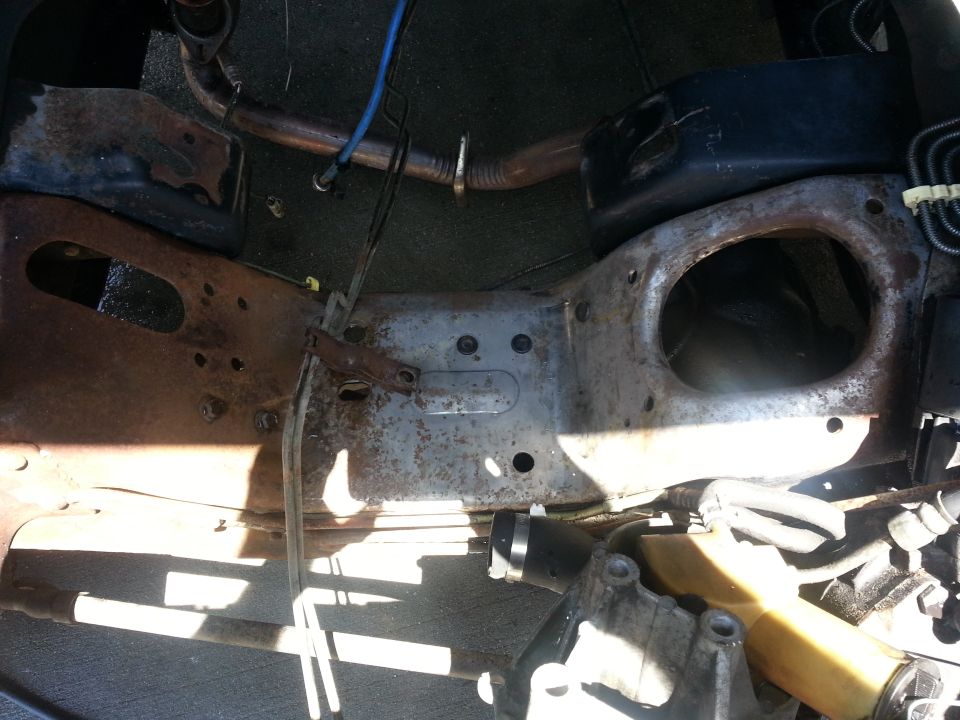 Engine bay frame with various hoses and metal components. A black plastic reservoir is visible