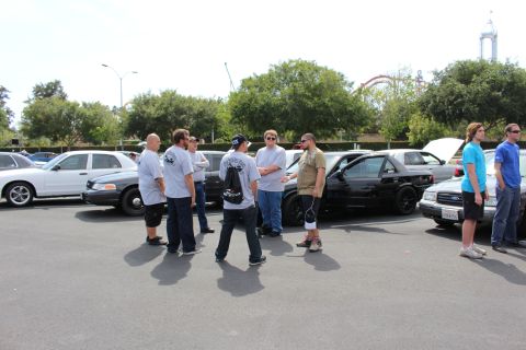 Group of men talking between rows of parked sedans at an outdoor car meet