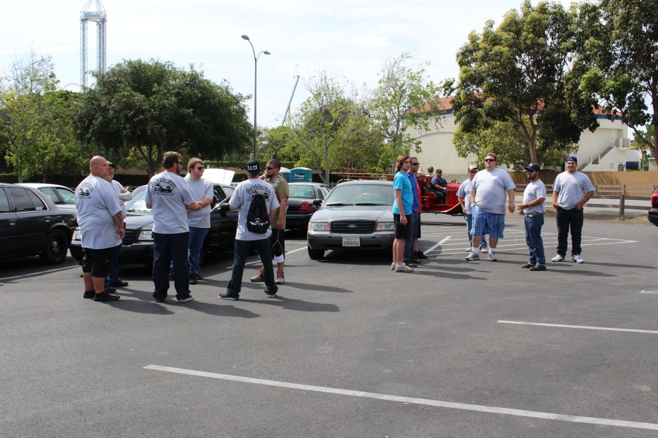 People standing in a parking lot among sedans with a red motorcycle visible