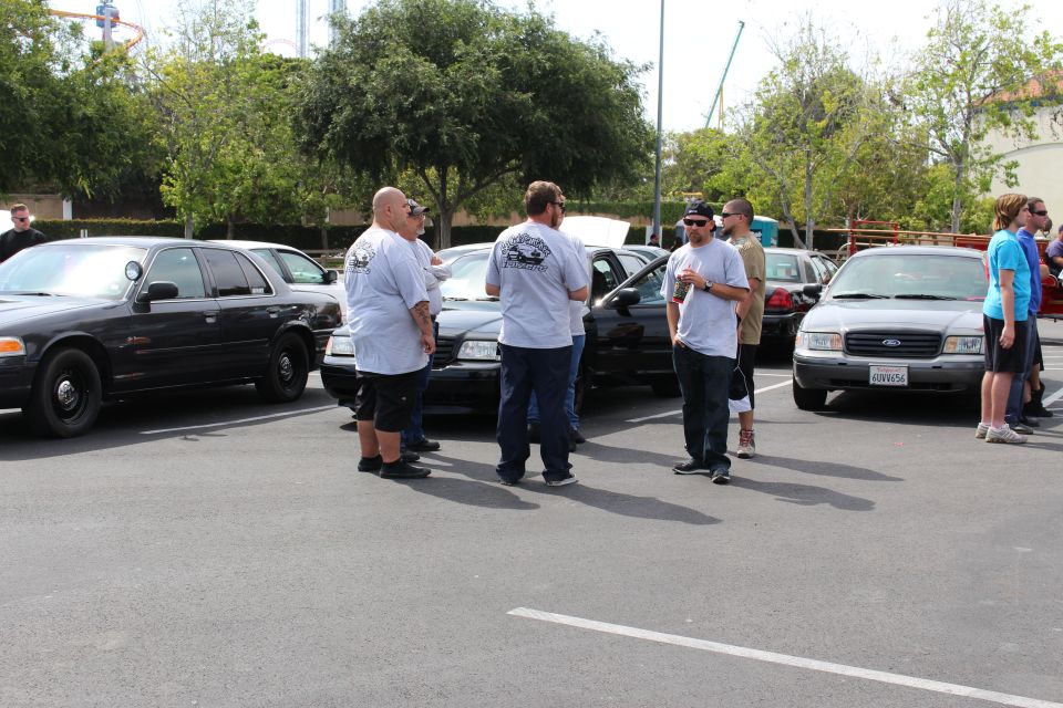 Men talking beside black and white Ford sedans at an outdoor meet