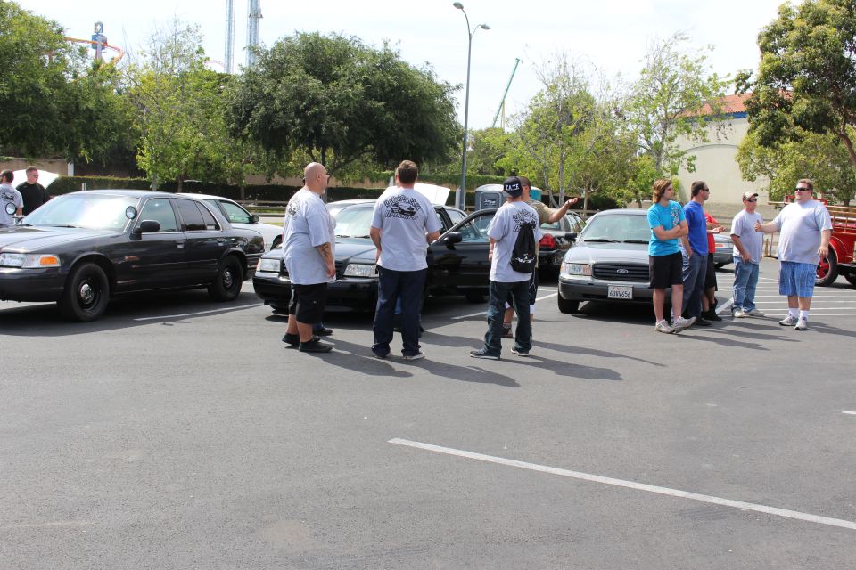 People standing between black and white Ford sedans at a parking-lot meet