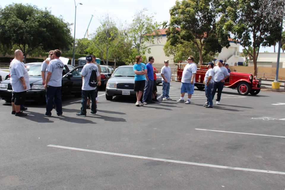 People near parked sedans with a vintage red fire truck on the right