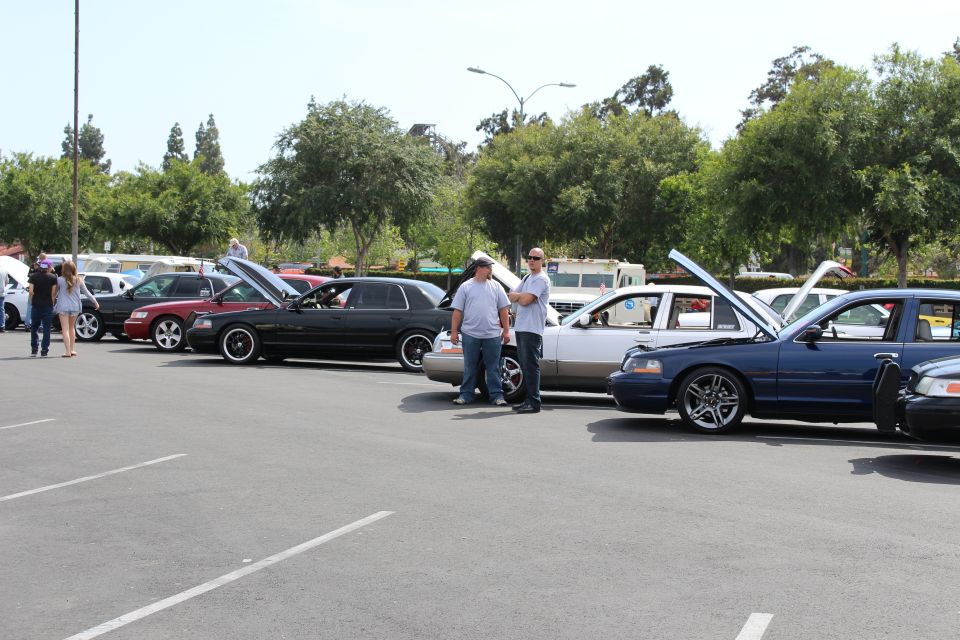 Two men standing beside a row of customized sedans with open hoods