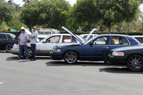 Two men beside a blue Ford sedan with open hood and chrome wheels